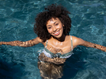 Portrait of a mixed race woman the swimming pool in the sun, looking up to camera smiling.